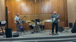 Half Step Trio on stage at Sunnybrook United Church: bass, drums and guitar in front of a wood-panelled wall.